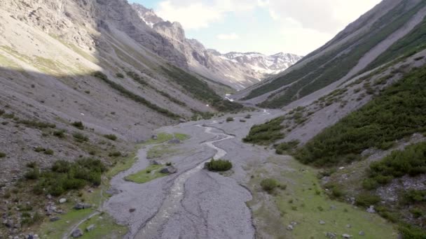 急峻な山々と松の木に囲まれた劇的な氷河の谷でゆっくりとねじれと下降する空中ドローン映像スイスの雪と高山川のパッチ — ストック動画