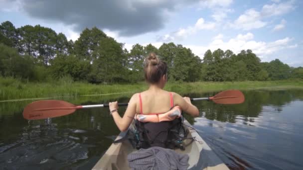 ブロンド女の子に彼女の背中にカメラPaddling Aカヤックでゆっくりと動きで川に囲まれた森 — ストック動画