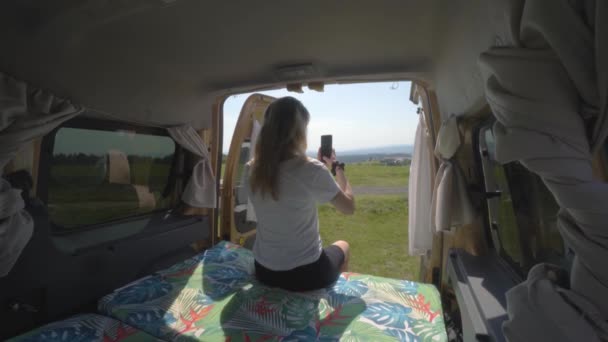 キャンパーバンの後ろから風景の電話で写真を撮るブロンドのデジタル遊牧民の女の子 — ストック動画