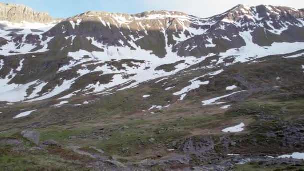 スイスの雪と高山草原の残りのパッチと劇的でギザギザの山の風景の中に高山草原の前方と近くに飛んで空中ドローン映像 — ストック動画