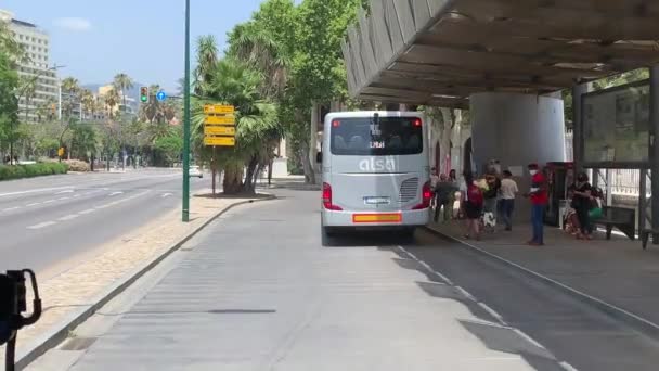 マラガのバス停にいる人たち 人々は顔のマスクを着ている スペインの都市の通勤者 マラガ港駅のバス停でスペインの人々をご覧ください 建物は背景にあります — ストック動画