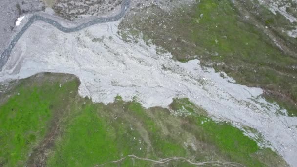 在瑞士山区 空中无人驾驶飞机的镜头缓慢地盘旋下来 滑向一个多风的灰色河床和一个长满青草的高山草甸 — 图库视频影像