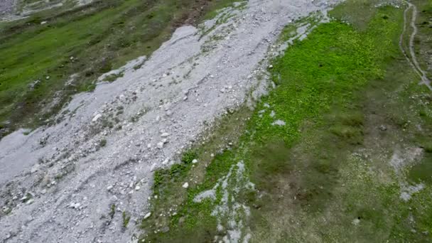 在瑞士 空中无人驾驶飞机的镜头缓缓倾斜 显示出一片高山草甸和草坡 周围是一片崎岖 冰封的山地景观 雪地斑斑 还有一条远足的小径 — 图库视频影像