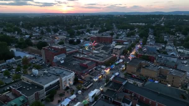 小都市アメリカの日没 ストリートフェア 夜のメインストリートでのカーニバルのライト 空中進入 — ストック動画
