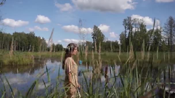 一个女人在池塘边走着 这时摄像机正站在她后面 前面是高草 颜色自然 动作缓慢 — 图库视频影像