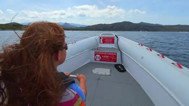 サルセチアの有名なビーチへのツアーのために北コルシカ海の水を航海するモーターボートにサングラス付きの長い髪の赤毛の子供のバックビュー スローモーション — ストック動画