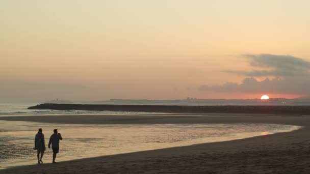 两名男性朋友在日落时在海滩上散步 射得很宽 — 图库视频影像