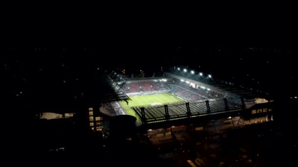 ファンでいっぱいの近代的なサッカースタジアムの空中ショットと洪水の光によって照らされた — ストック動画