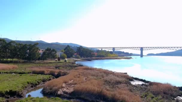 位于西班牙加利西亚Catoira的Ulla河上的铁路桥 岸上的树木和房屋 树木繁茂的山岗 背风涡轮机 无人驾驶飞机在空中盘旋 — 图库视频影像