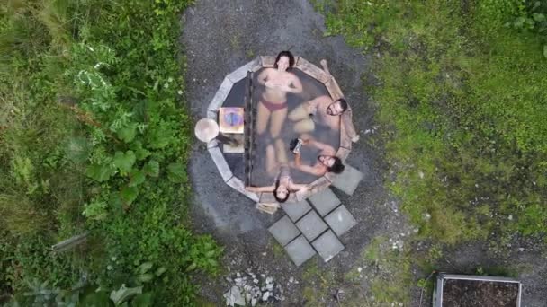 上升的空中景观 直接超过四个年轻人坐在一个私人花园的热浴缸里在一个多风的日子 看着镜头 — 图库视频影像