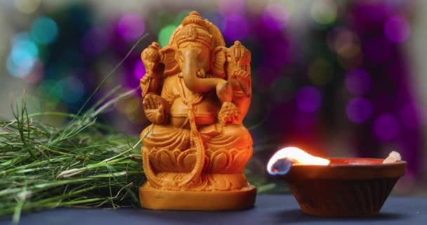 ガネーシュ チャトゥティの祭りの間に ヒンズー教の神ガネーシャの手作りの粘土の偶像の横で明るく燃えるカラフルなディヤのショットを閉じます — ストック動画