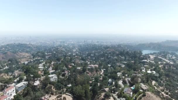 ハリウッド ヒル上空を空中に移動する中高度 ヘイズは地平線の風景のほとんどをカバーしています 木々の中からは上から家やプールや道路が見える — ストック動画