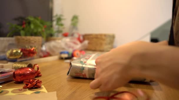 用繁文缛节包裹圣诞礼物 用剪刀和薄薄的繁文缛节做一个弓 用圣诞装饰纸和彩带把礼物包在桌上 你自己动手吧 — 图库视频影像