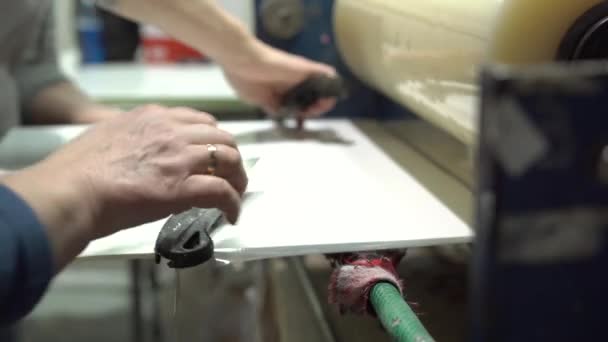機械から出てくる葉っぱ状のガラス 労働者はナイフで余分な箔を切断している 壊れないガラスだ 温度の高いガラスプロセス 安全ガラス — ストック動画