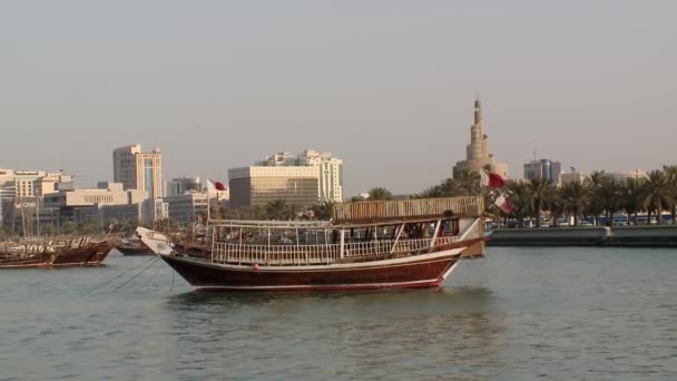 カタールのドーハの内側の港に停泊しているアラブのダウ船は 象徴的なミニチュアとモダンなドーハのスカイラインを眺めます — ストック動画