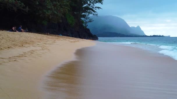 左のビーチで数人の人々のHdハワイカウアイゆっくりとした動き海の波が右から左に向かってくるパフ マジック ドラゴン ハナレイ Honah Lee 遠くの山岳海岸線 — ストック動画