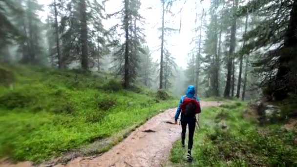 雹と激しい雨の歩道が泥だらけの水であふれている嵐の中で下り坂のハイキングに若い女性の後 — ストック動画