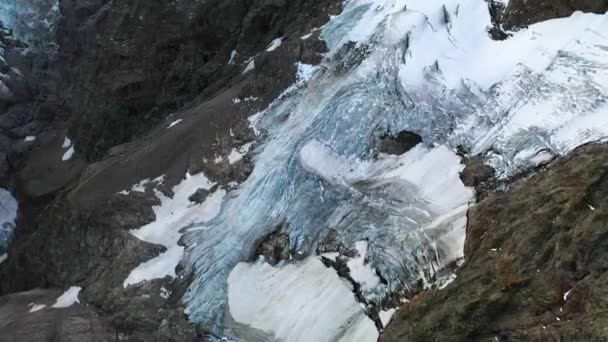 無人偵察機はほとんどなくなっている溶けた氷河の上に撃ちました 裸と岩の山の中腹の横に雪と自然のパターンや形状を持つ青の氷 スイスアルプスの急な坂 — ストック動画