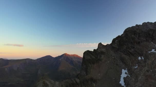 空中射击缓慢地降落在山脊悬崖旁边 蓝蓝的天空 红色和橙色的日出与远方的山峰相接 安静和沉默的性质 — 图库视频影像