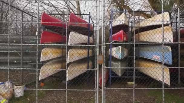 市所有の公園で秋のシーズンオフ時にロックされたフェンスの後ろに整理積み上げカラフルなカヌーを保存 — ストック動画