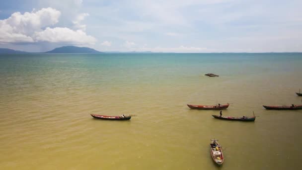 東南アジア沖の砂浜の青い海に小さなボートを準備する漁師 水平線と島を背景にドローンが飛び立つ — ストック動画