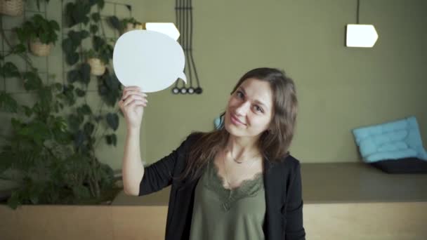 学生ブルネットの髪の女性ヨーロッパの学生は テキスト対話を記述するために雲の矢印を指す カメラを見て笑顔を奨励します 緑の背景を持つ現代の教室に立つ肖像 — ストック動画
