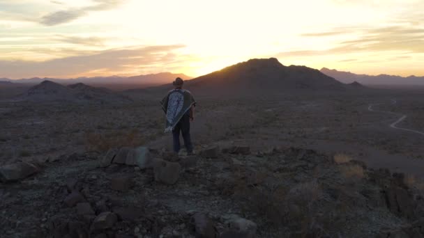 当太阳落山的时候 一个身穿狂野西部英雄服装的斗篷矗立在西南的山顶上 眺望着一片崎岖的沙漠风景 照相机使空中的人偶运动起来 — 图库视频影像