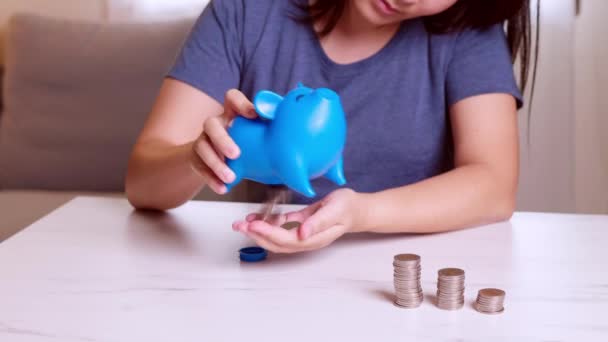 女性の手を拾うコインで青い貯金箱の中に空白のメタファーを使って支出と貯蓄のための別の種類のお金 — ストック動画