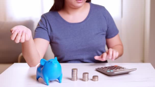 女人用计算器 把钱币放进蓝色的储蓄罐里 用空白的比喻表示不同种类的钱用于消费和储蓄 — 图库视频影像