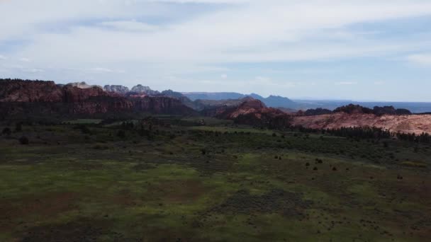 遠くの景色を望む山々に囲まれた谷の茂みや木と緑の平野と雲と青い地平線 シオン国立公園ユタ上空の無人機からの後退する眺め — ストック動画