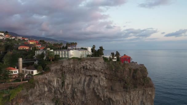 ドローンは上に移動して傾斜し 島の上に嵐の雲が来ると日没の最後の瞬間にマデイラのポンタ ソルの崖の上の高級ホテルを見下ろします — ストック動画