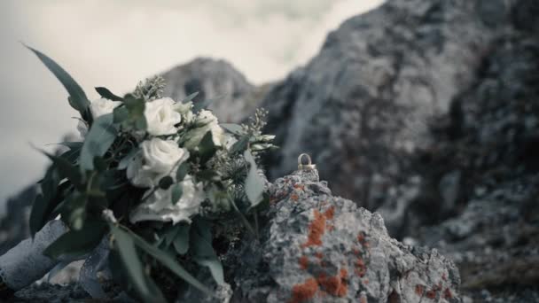 当风吹着树叶的时候 缀着白玫瑰和金戒指的新娘花束躺在阿尔卑斯山山顶的岩石上 — 图库视频影像