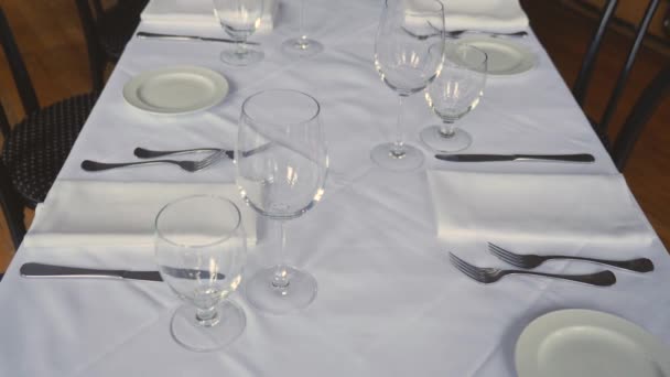 高級レストランでの結婚式や企業イベントのためのダイニングテーブルセットセラミックプレートは テーブルの上に白いテーブルクロスにナイフ布ナプキンをフォーク安定したスローモーション中タイト — ストック動画