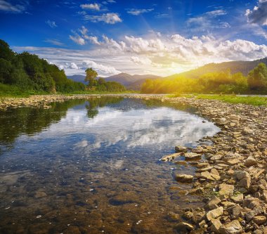 Gün batımında dağlara doğru uzanan kayalıklı berrak bir nehir.