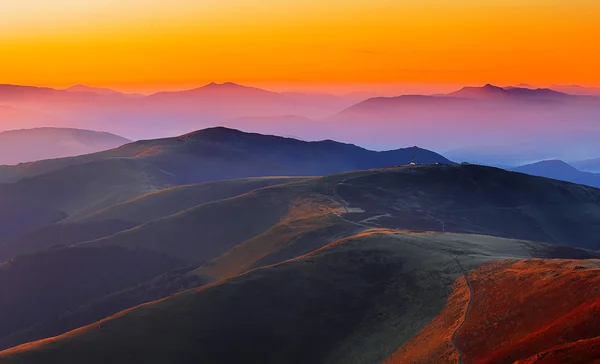 Winding road through meadows of  mountain range at sunset — Stock Photo, Image