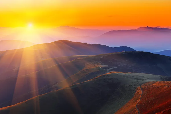 Winding road through meadows of  mountain range at sunset — Stock Photo, Image