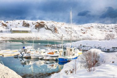 Küçük bir balıkçı köyünde yatları ve tekneleri olan dramatik kış manzarası ve Valberg yakınlarındaki karlı dağ zirveleri. Konum: Valberg, Vestvagoy, Lofotens, Norveç