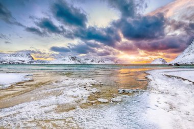 Gün batımında Haukland plajı ve Leknes yakınlarındaki karlı dağ zirveleriyle muhteşem bir kış manzarası. Konum: Leknes, Vestvagoy, Lofotens, Norveç