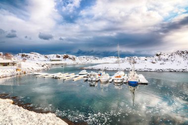Küçük bir balıkçı köyünde yatları ve tekneleri olan dramatik kış manzarası ve Valberg yakınlarındaki karlı dağ zirveleri. Konum: Valberg, Vestvagoy, Lofotens, Norveç
