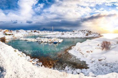 Küçük bir balıkçı köyünde yatları ve tekneleri olan dramatik kış manzarası ve Valberg yakınlarındaki karlı dağ zirveleri. Konum: Valberg, Vestvagoy, Lofotens, Norveç