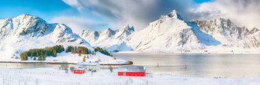 Güneşli bir günde Selfjorden 'da panoramik kış manzarası, küçük balıkçı evleri (rorbu) ve arka planda karlı zirveler. Konum: Flakstadoya Adası Lofoten; Norveç, Avrupa