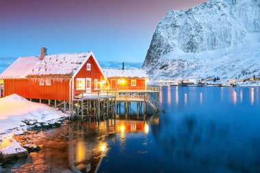 Arka planda karlı bıyıkları olan Reine kasabasının muhteşem gece manzarası. Lofotens 'ta popüler bir seyahat yeri. Konum: Reine, Lofoten; Norveç, Avrupa