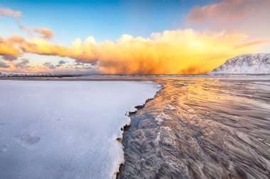 Skagsanden sahilinde güneş doğarken aydınlık bulutların olduğu şaşırtıcı kış manzarası. Popüler turizm merkezi. Konum: Flakstadoya Adası, Lofoten; Norveç, Avrupa