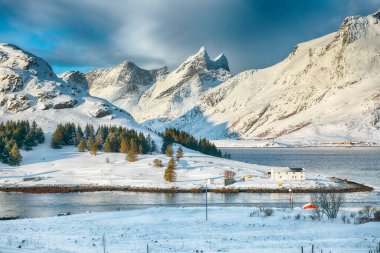 Arka planda küçük balıkçı evleri (rorbu) ve karlı zirveleri ile Selfjorden 'da şaşırtıcı kış manzarası. Konum: Flakstadoya Adası Lofoten; Norveç, Avrupa