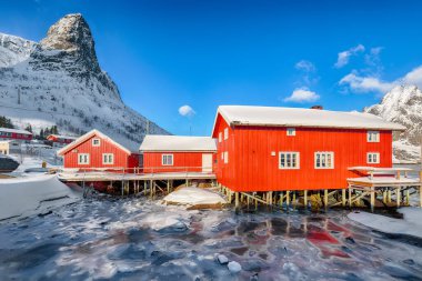 Reine Village ve Gravdalbukta Körfezi 'nde kışın güneşli manzarası var. Arka planda karlı dağ zirveleri. Konum: Reine, Lofoten; Norveç, Avrupa