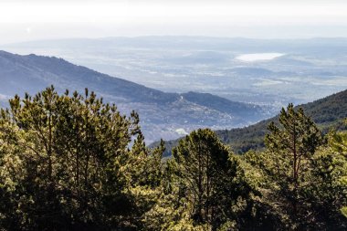 Vadinin üzerindeki yeşil manzara, ağaçlar, kayalar ve ufuktaki dağlar. La Morcuera, Navacerrada, Madrid. Avrupa.