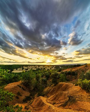 Tarlada günbatımı manzarası, ağaçlar, kırmızı toprak ve gökyüzü... Alacakaranlık mavi ve turuncu tonlarda büyük bulutlar. Geniş açı, panoramik fotoğraf. İspanya.
