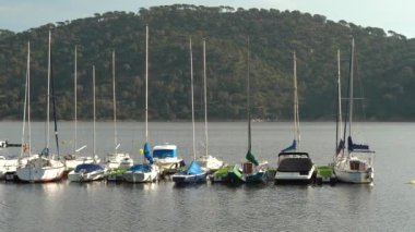 Günbatımında göldeki rıhtıma yanaşan yelkenli teknelerinin arka planında yeşil dağlar ve gün batımının altın rengi vardı. Pantano de San Juan, Madrid.