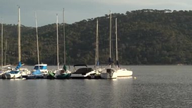 Günbatımında göldeki rıhtıma yanaşan yelkenli teknelerinin arka planında yeşil dağlar ve gün batımının altın rengi vardı. Pantano de San Juan, Madrid.