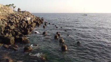 Sahilde dalgaların kırıldığı kayalık sahilin ve arka plandan geçen yelkenli gemisinin havadan görüntüsü. Büyük Kanarya. İspanya.